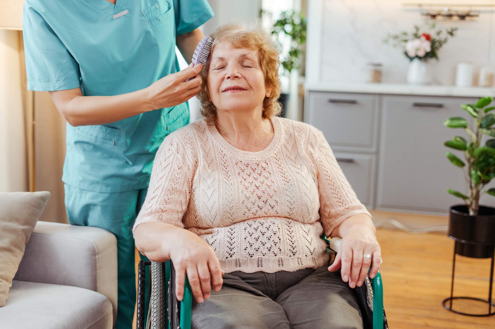 Nurse brushing hair of elderly woman in wheelchair smiling